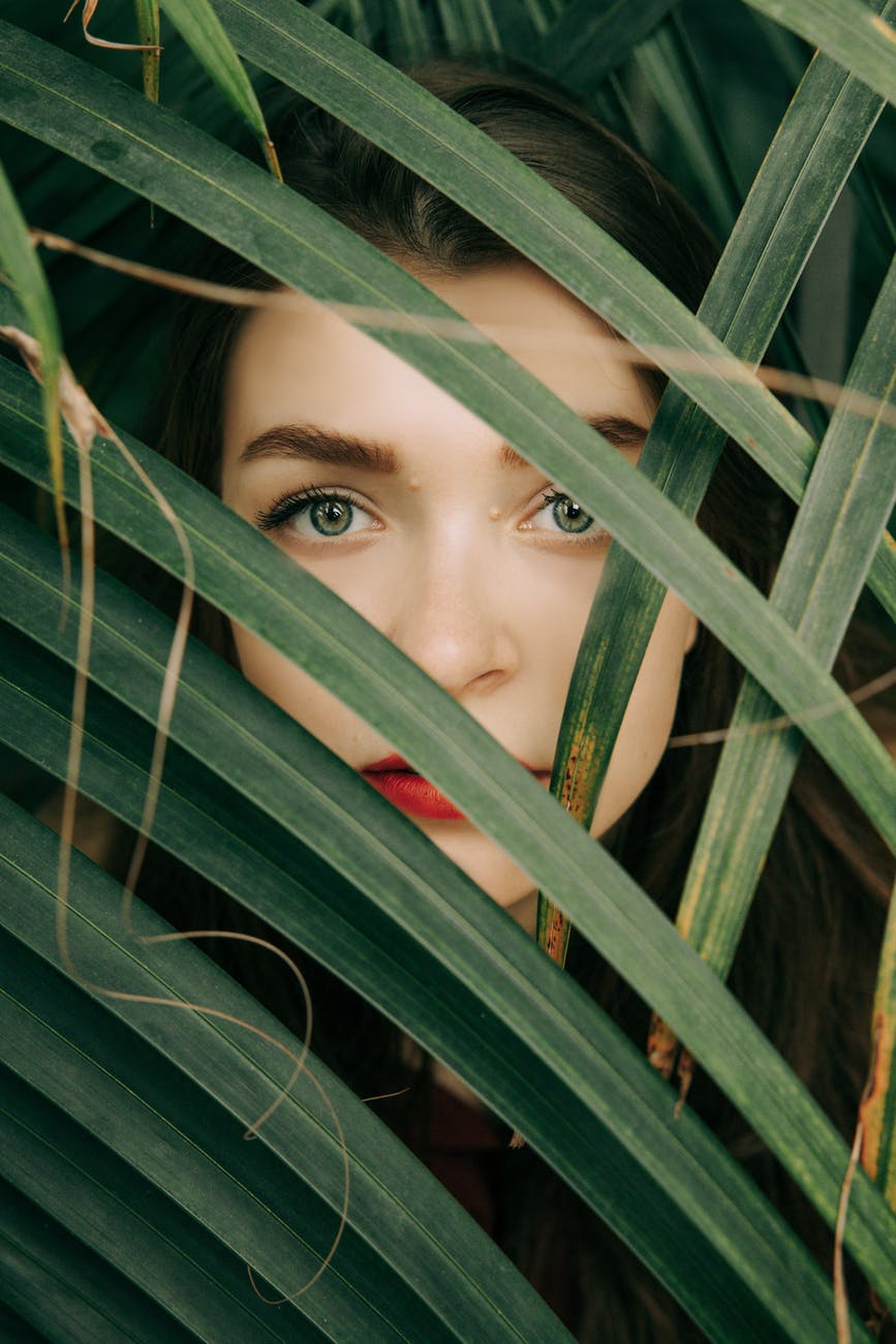woman in red lipstick hiding behind green leaves