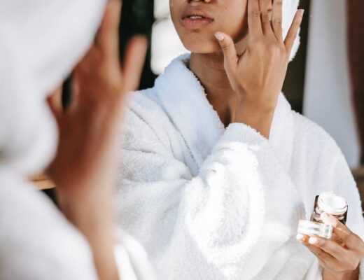 black woman with towel applying cream on face